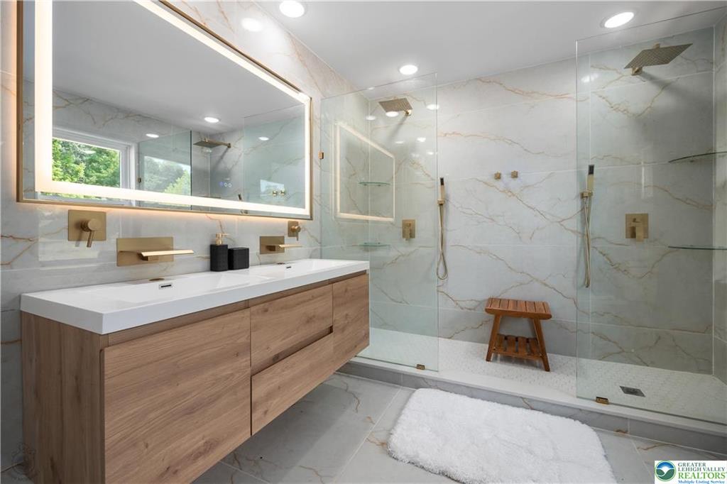 Luxury bathroom with marble tile, gold fixtures, and floating wood vanity