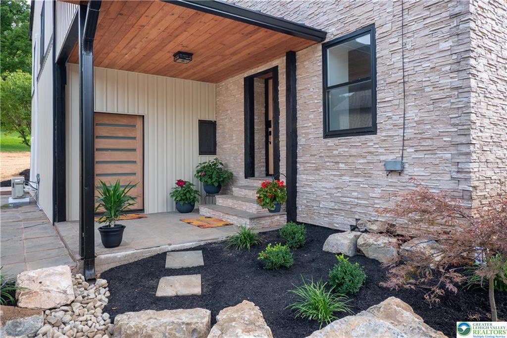 Modern wood front door framed by stacked stone and board-and-batten siding
