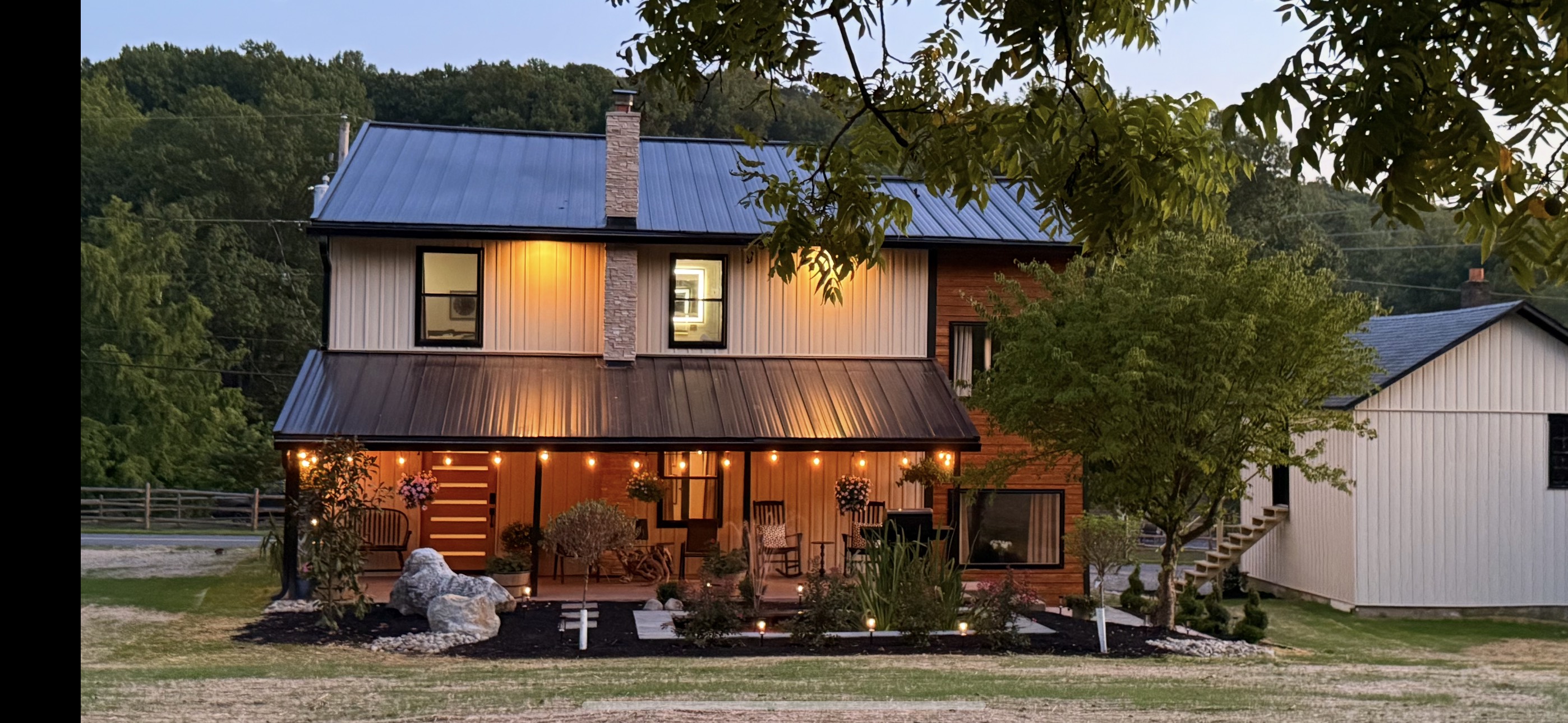 Custom barndominium home at dusk with covered porch, string lights, and metal roof built by East Coast Homes in Hellertown, PA