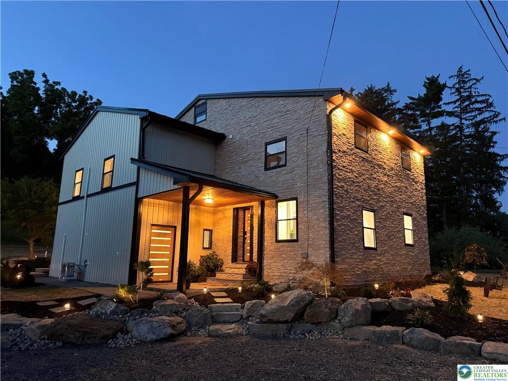 Front exterior of the Hellertown barndominium at twilight with stacked stone facade and lit wood entry