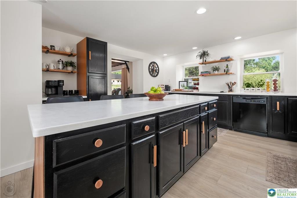 Kitchen with black cabinets, white countertop island, and open wood shelving