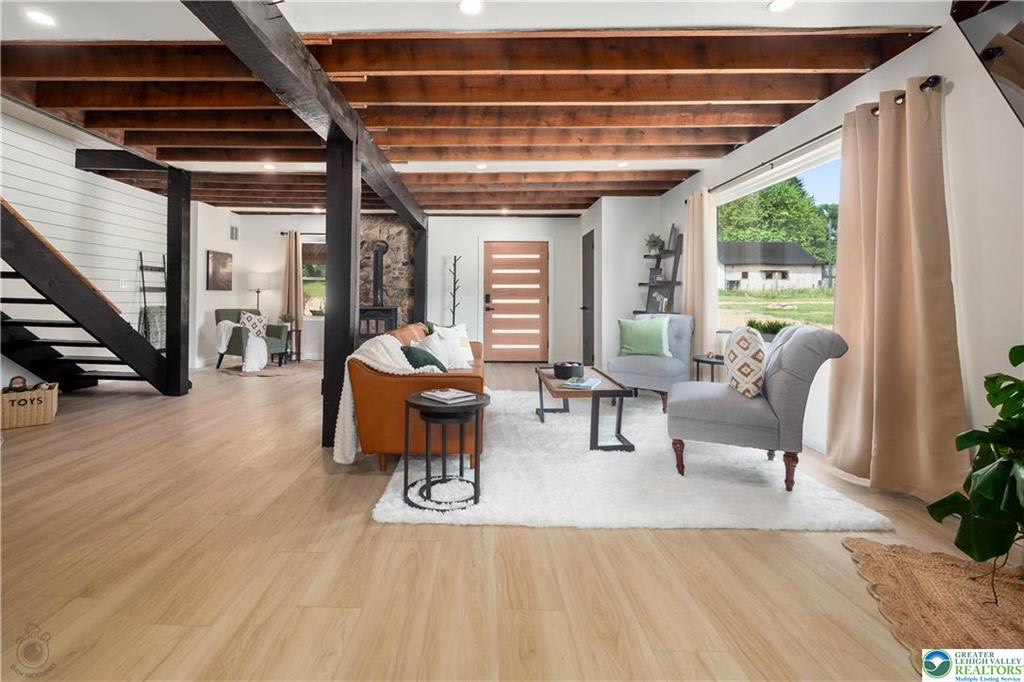 Open living room with exposed wood beams, black posts, and staircase