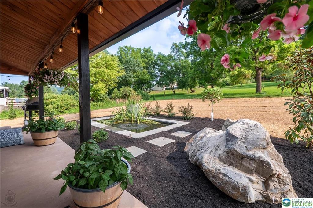 Covered porch overlooking landscaped yard with water feature and potted plants